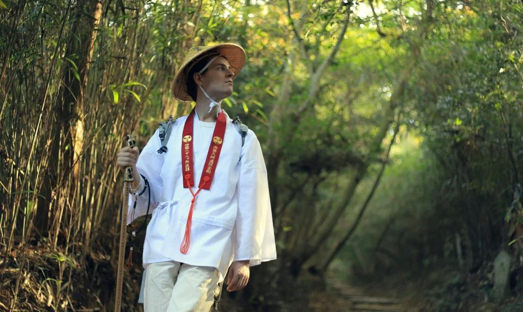 A pilgrim walking on the Shikoku Henro, wearing a traditional white outfit with a straw hat and walking stick