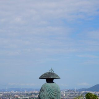 A statue of a monk overlooking an urban landscape under a blue sky: Shikoku Henro trail