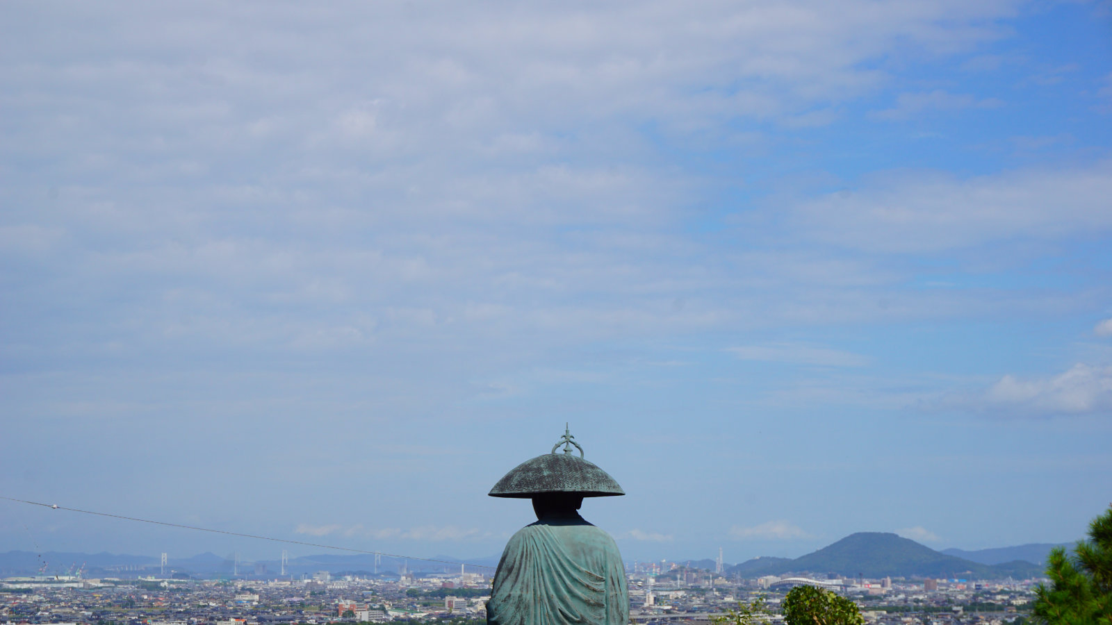 A statue of a monk overlooking an urban landscape under a blue sky: Shikoku Henro trail