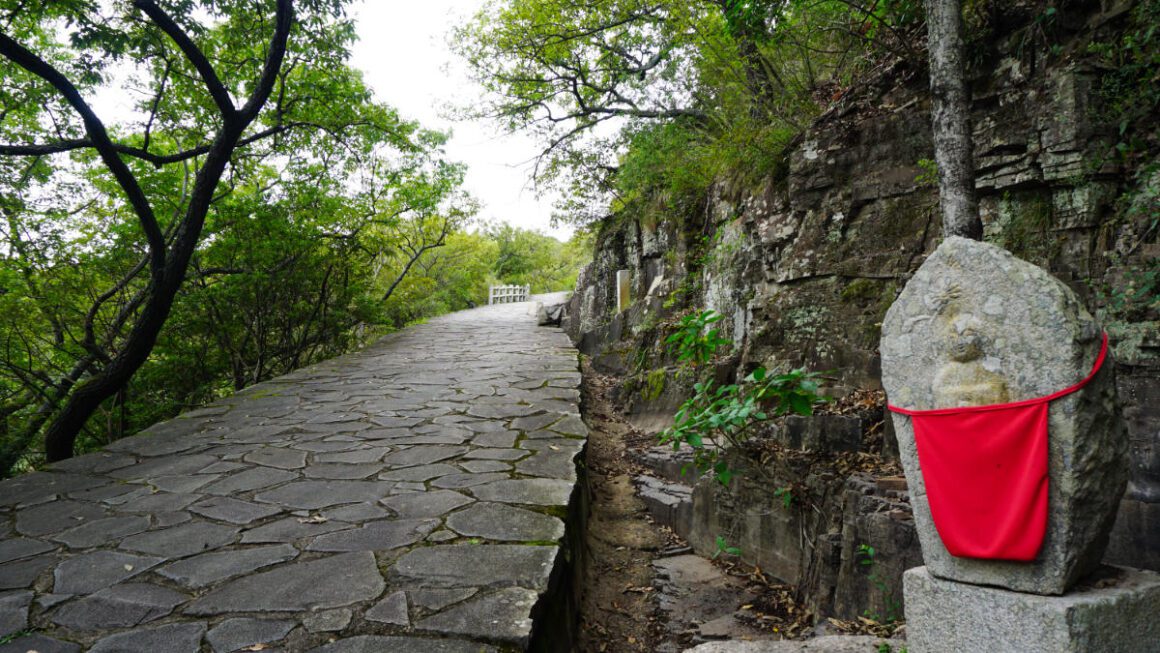 A stone path going uphill, with a buddha statue in the foreground